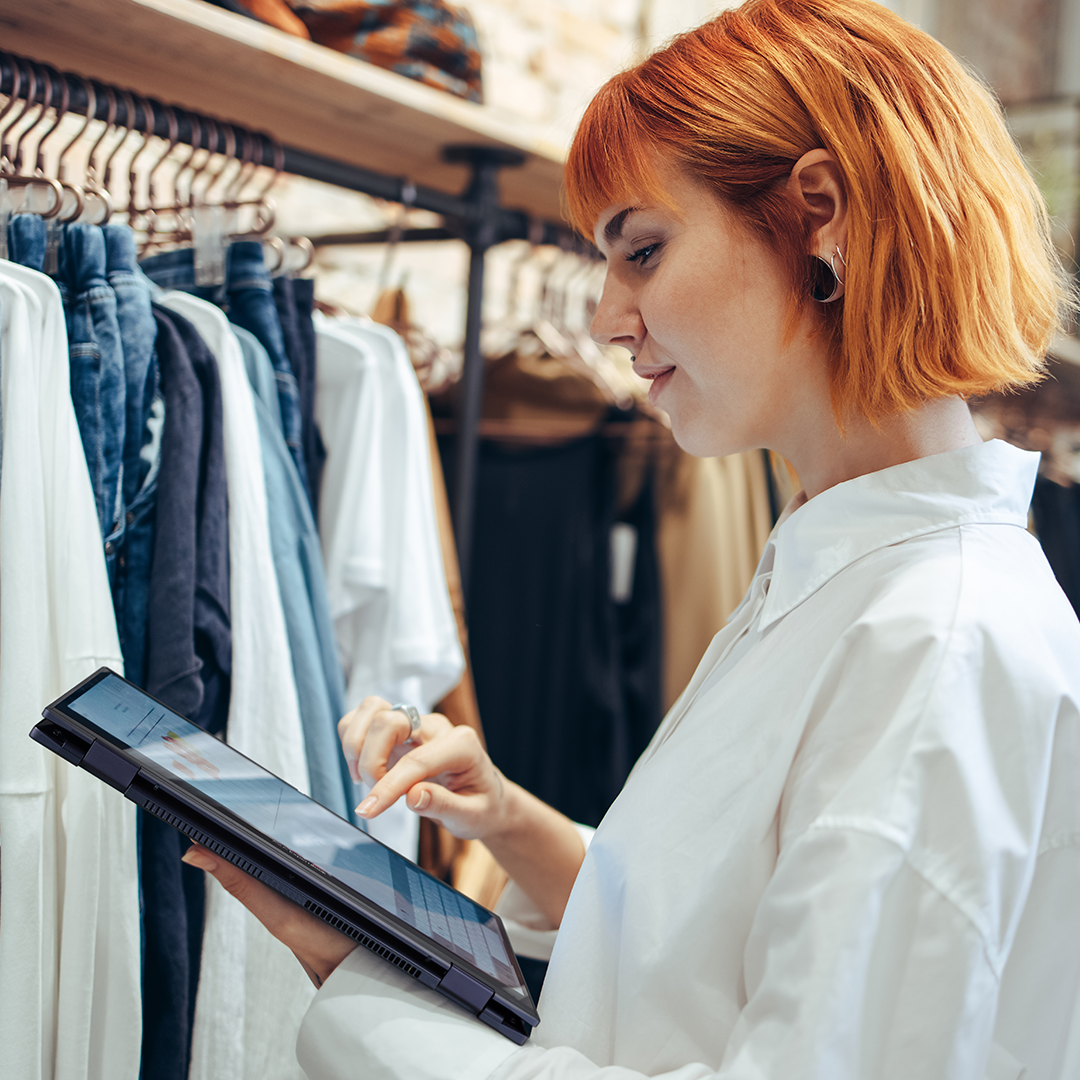 A cloth store staff is looking at ASUS ExpertBook B5 Flip in tablet mode in the store.