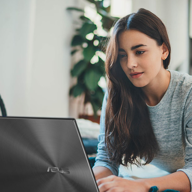 young casually-dressed woman lying on the ground at home using ASUS Zenbook 14X OLED laptop?