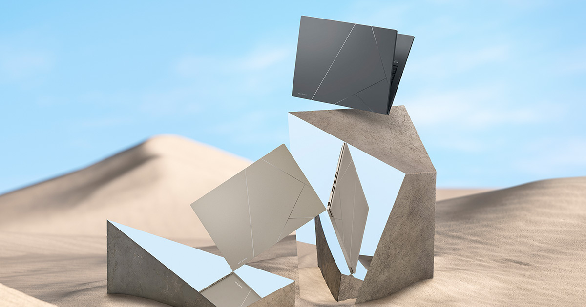 two ASUS Zenbook 14X OLED laptops in Sandstone Beige and Inkwell Gray balancing on a modern mirror-like geometric structures placed in the middle of a sand dune, with clear blue sky in the background