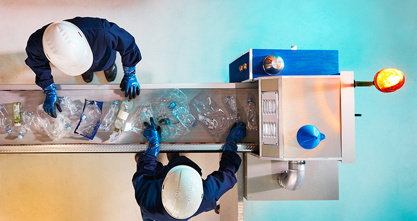 two workers sorting bottles on a conveyor belt for recycling