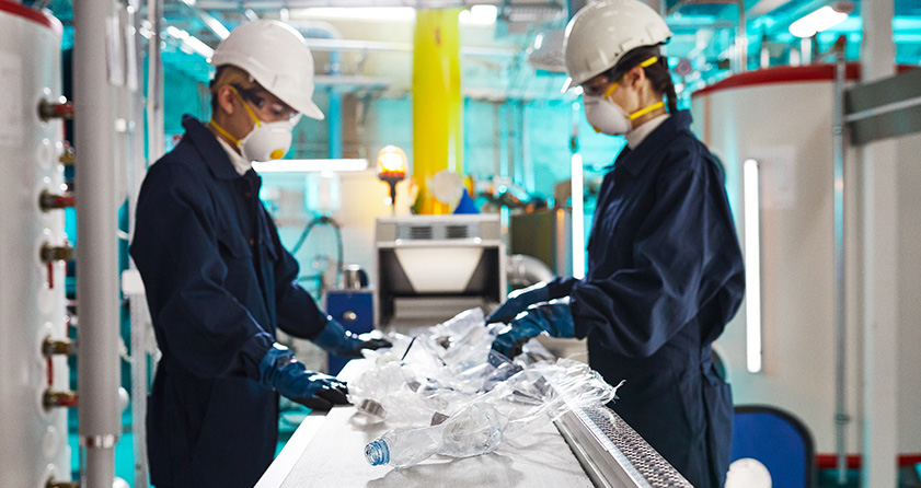 two workers sorting plastic bottles on a conveyor belt on a manufacturing line