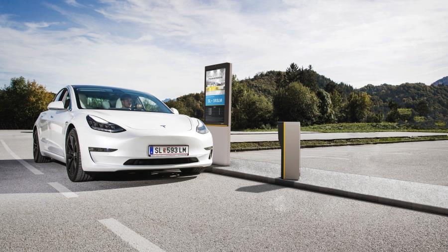 A male is driving an electric vehicle through a digital entrance gate at smart outdoor parking lot with car and parking information shown on gate signage board