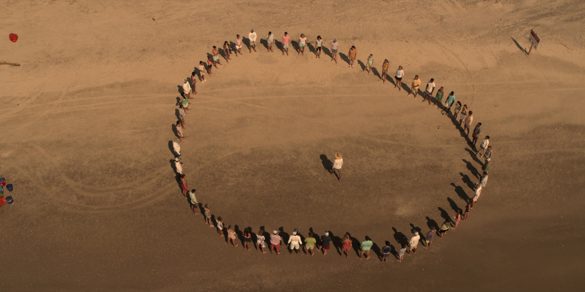 Bird's-eye view shot of the Kooks standing in a circle on the beach.