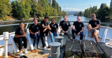 seven people sit on the front of a boat on the water