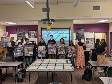 A dozen MESA students standing at the front of a classroom, and showing their "vision boards"