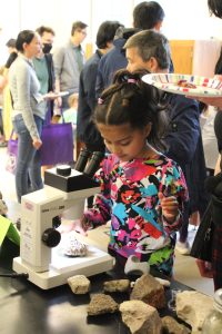 A young kid looks at a rock through a microscope.