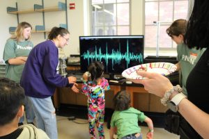 A kid jumps up and down to see their jumps recorded by a seismometer and displayed on a screen.