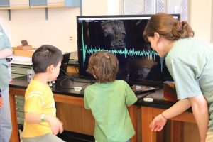 Two kids jump up and down to see their jumps recorded by a seismometer and displayed on a screen.