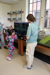 A kid jumps up and down to see their jumps recorded by a seismometer and displayed on a screen.