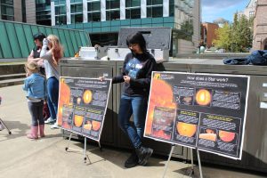 Graduate student Ula Jones standing between two posters talking about the sun. One poster is in English and the other is in Spanish.