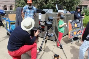 A kid looks through a telescope with Professor Baptiste Journaux to see the sun's surface.