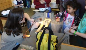 Two kids watching the regelation of ice demo, where a wire with two weights on either side cuts through a core of ice, leaving the ice intact behind it.