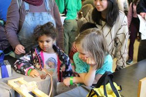 Two kids watching the regelation of ice demo, where a wire with two weights on either side cuts through a core of ice, leaving the ice intact behind it.