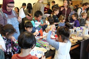 Young kids stand with their parents or guardians at a table paining their own pet rocks to take home.