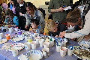 Young kids stand with their parents or guardians at a table paining their own pet rocks to take home.