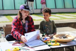 A young kid sits with a graduate student, picking a geoscience-themed coloring sheet out of a binder.