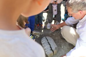 A group of kids with Professor John Stone, standing around a large rock that was just split down the middle.