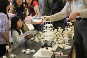 A young kid builds a structure with marshmallows and sticks. The structure sits on a plate that moves, simulating an earthquake.