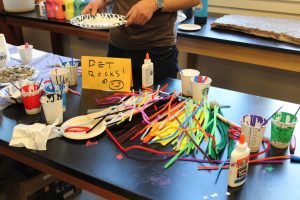 A table of crafts, including paint, googly eyes, and pipe cleaners to make your own pet rock.