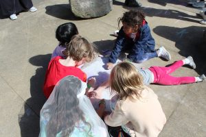 A group of five young kids working together to color in a crystal with chalk.