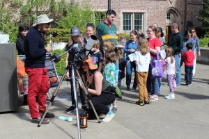 Kids and adults line up outside to look into a telescope to see the sun's surface.