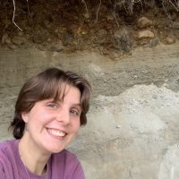 Short haired student smiling at the camera in front of a wall with different horizontal layers.