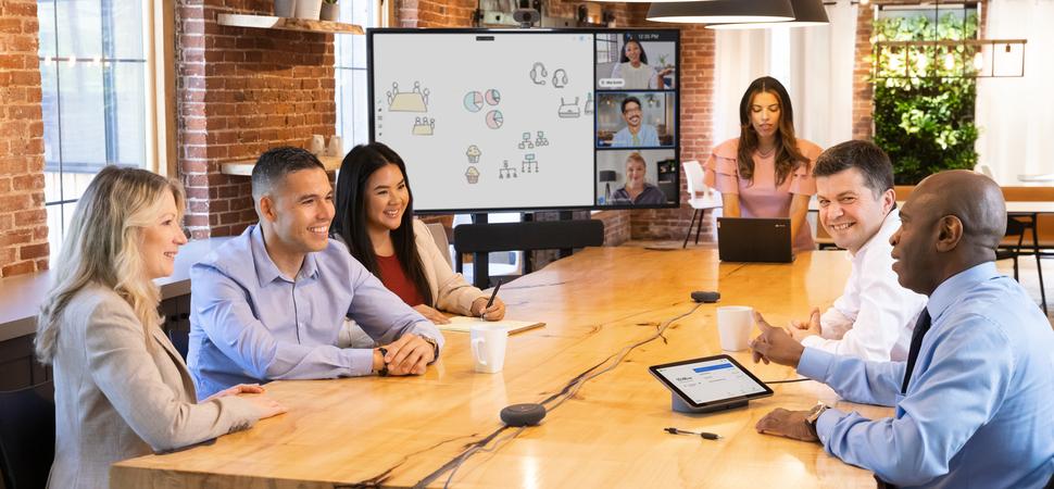 An image of a group of people in a meeting room with a Google Meet Series One Large Room mounted to an AV cart at the head of the table.