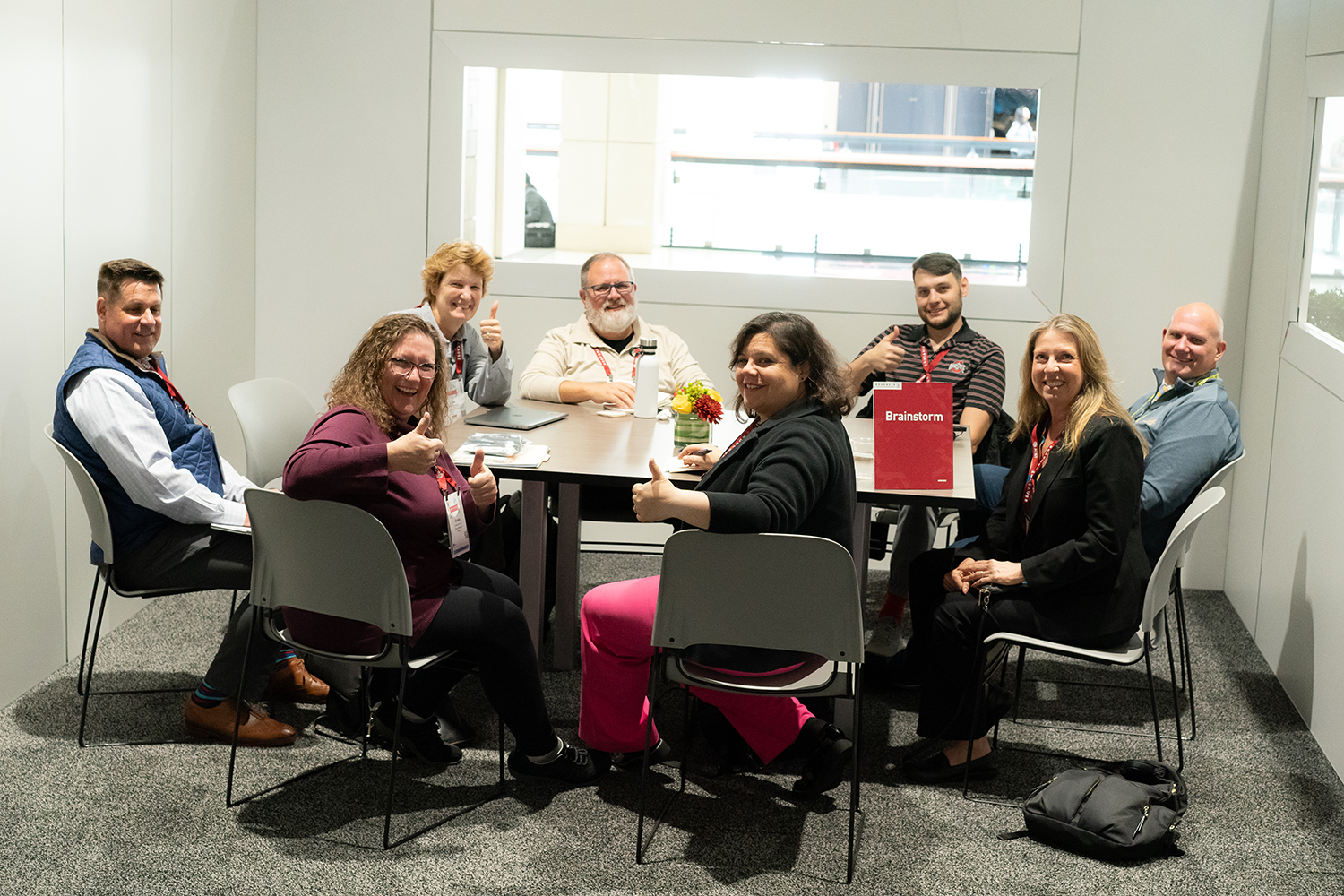 Group sitting around a table. Many are giving a thumbs up.