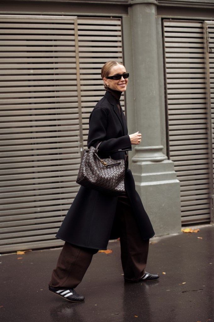 Pernille Teisbaek wears wide brown pants, black turtle neck top and long jacket, sunglasses and dark brown bag outside The Courreges show d in Paris, France. 