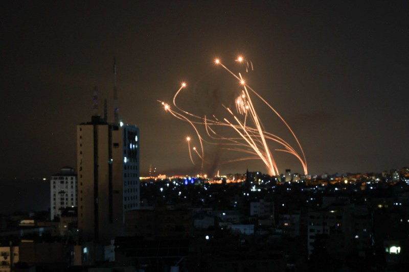 Bursts of light fly over a city skyline at night, showing the path of a missile fired from Israel's Iron Dome air-defense system as it intercepts another missile.