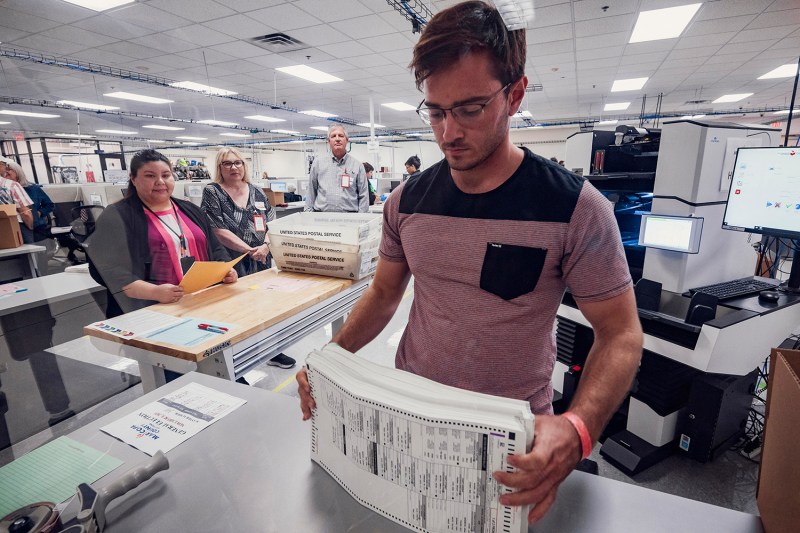 An election worker processes a stack of 2024 general election ballots with the tabulation machine in front of observers.