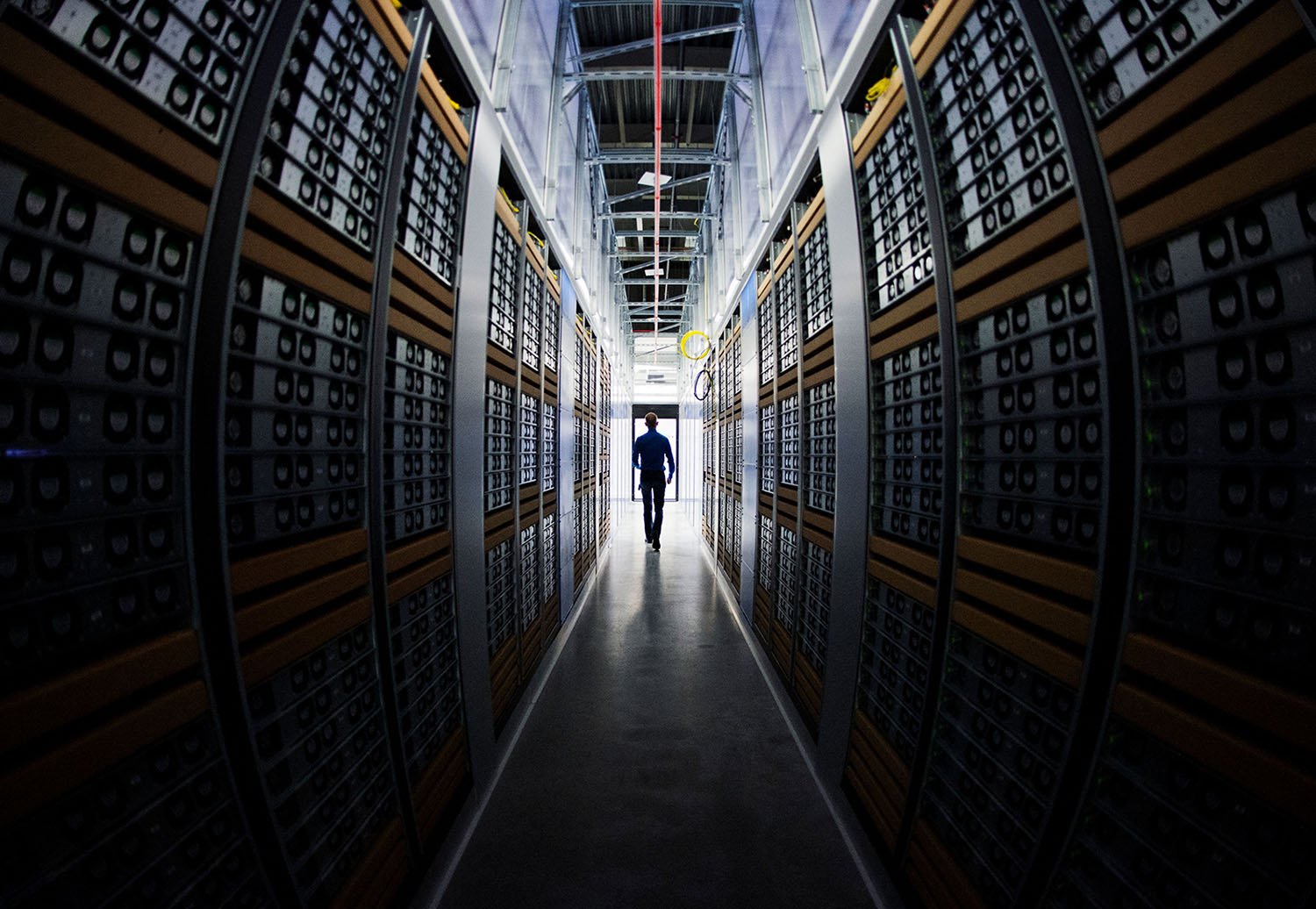 A person is silhouetted at center down a long dark aisle of servers.