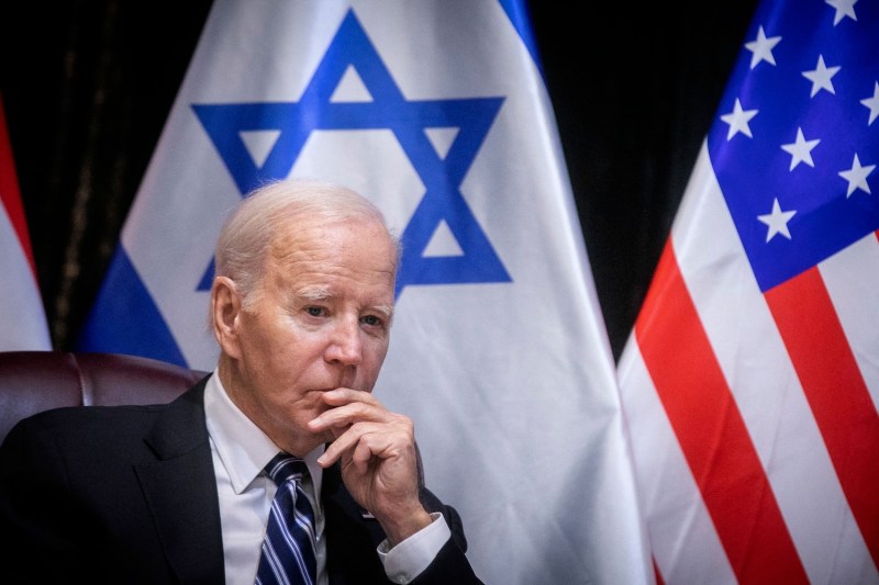 Biden looks pensive as he sits in front of Israeli and U.S. flags.