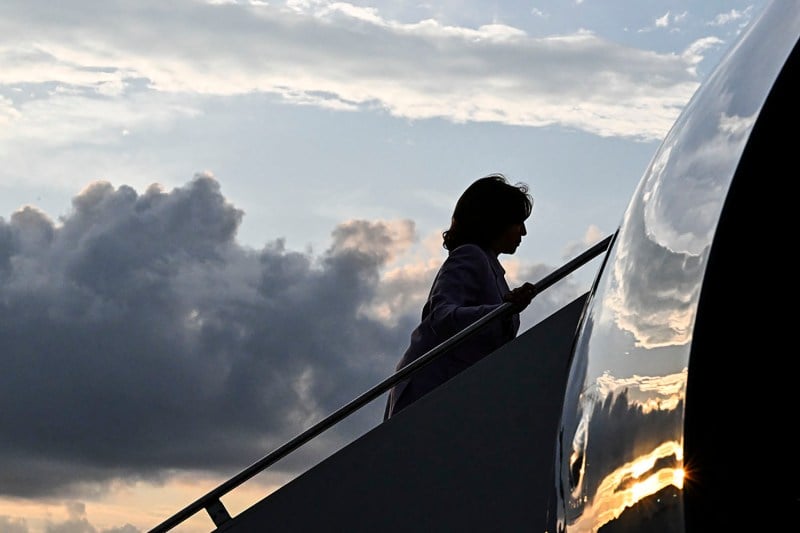 Kamala Harris is silhouetted against a cloudy sky at sunset as she walks up the steps of a plane.