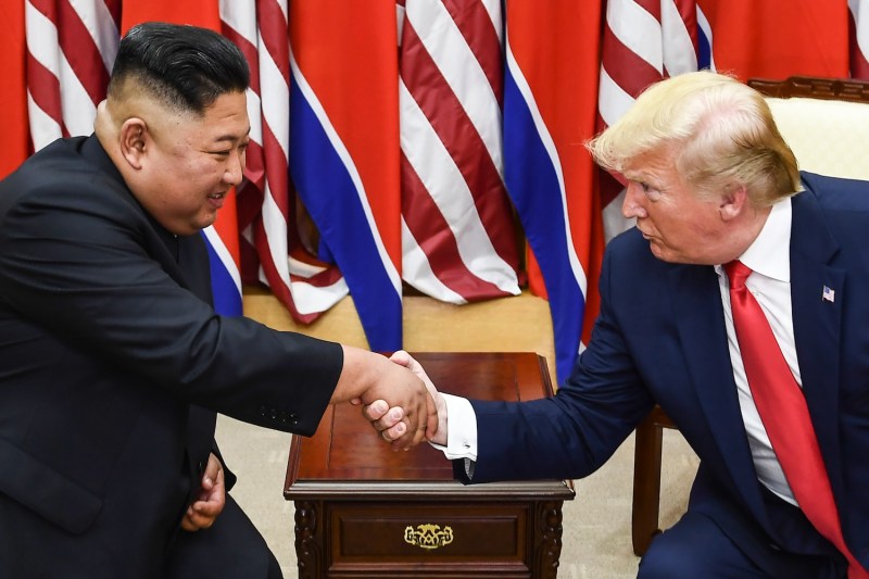 North Korean leader Kim Jong Un and U.S. President Donald Trump shake hands with North Korean and U.S. flags behind them.