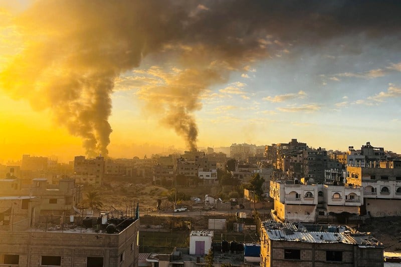 Smoke billows on an orange-hued horizon over the devastated landscape of the Gaza Strip.