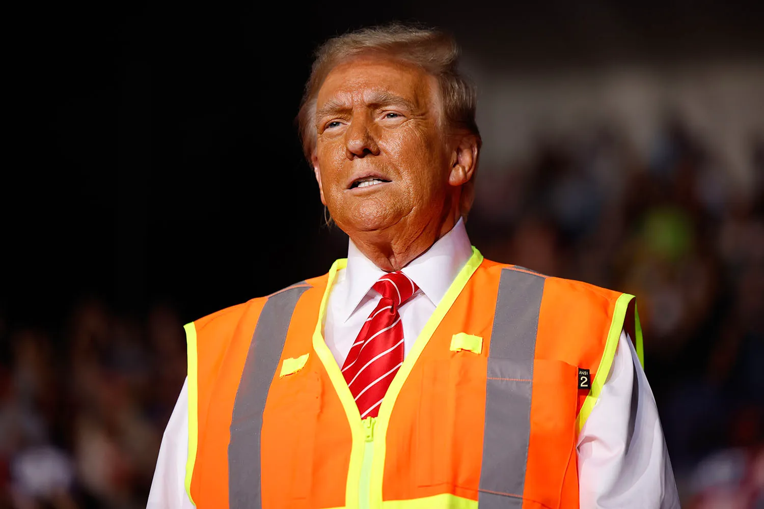 Donald Trump wears a button-up suit and tie with an orange construction vest over it.