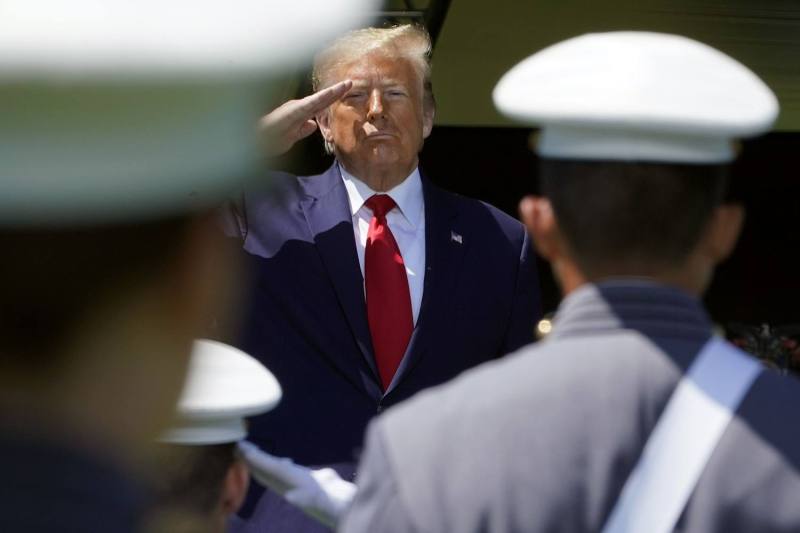 Donald Trump salutes U.S. military cadets, who are seen from behind in their formal dress uniforms as they face him.