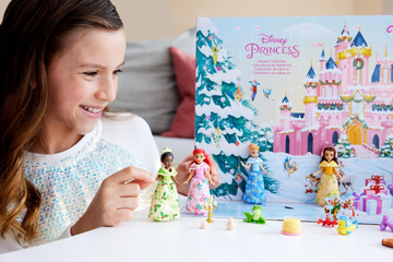 a child is interacting with an advent calendar themed around disney princesses the calendar features a colorful backdrop of a castle and a winter scene several small collectible figures of princesses including characters in colorful dresses are placed on a white table alongside the figures are various small accessories and toys such as a frog a cake and other themed items related to the series the scene conveys a festive and playful spirit