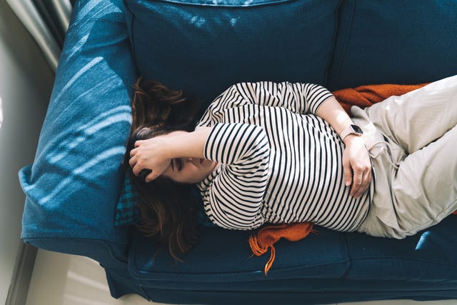 woman clutches her stomach while lying on a couch