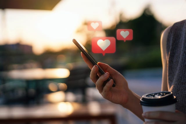 close up of young woman checking social media network on smartphone on the go in the city mobile phone with heart emoji speech bubble message on the screen people engaging in networking with technology social media addiction concept