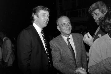 roy cohn shaking a hand as donald trump stands to his right smiling