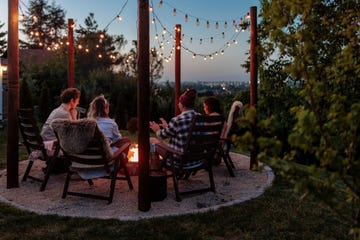 four people sitting next to a burning fire pit at sunset