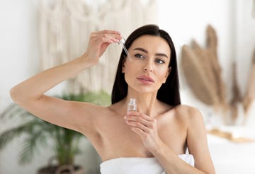 modern beauty products at home, cosmetology, anti aging cosmetics and advice from blogger and specialist young brunette lady in towel applies oil to skin of face, on bedroom interior background