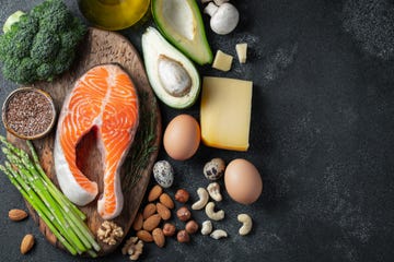 A set of healthy food for keto diet on a dark background. Fresh raw salmon steak with flax seeds, broccoli, avocado, chicken eggs, nuts and asparagus on a wooden Board. Top view with copy space