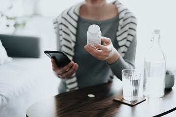 close up of young asian woman holding a pill bottle, consulting to her family doctor online in a virtual appointment over the smartphone at home