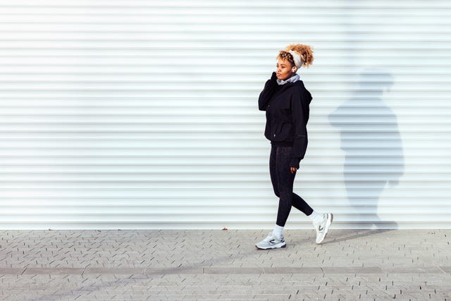 beautiful female athlete in black sportswear, walking outside next to the white garage door on a bright sunny day