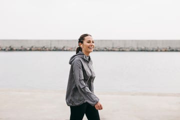 Person walking by the water in a gray jacket and earphones