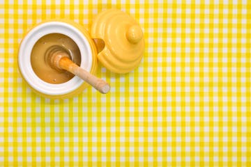 Manuka Honey pot and dipper on yellow background with copy space.