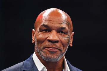 boxing champion mike tyson smiles and looks past the camera, he wears a blue suit jacket and white collared shirt